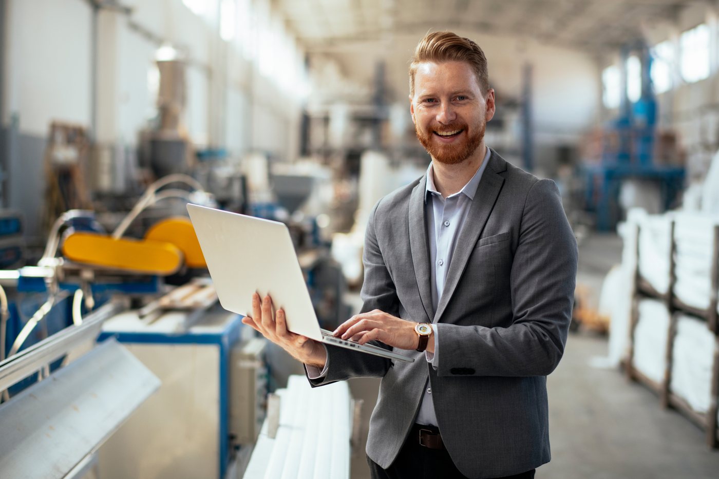 A smiling engineer holding a laptop on a plant floor