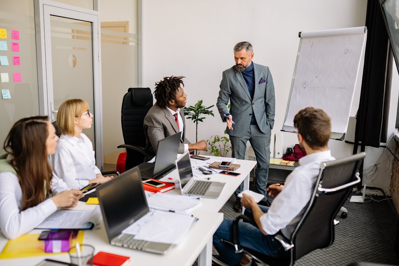 A presenter at a flip chart with a team seated around a conference table