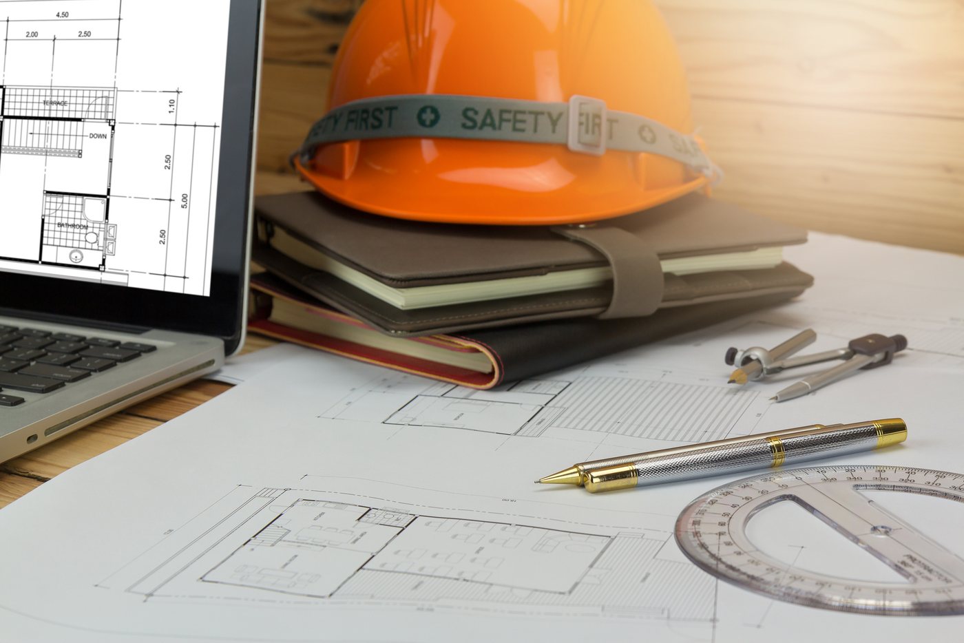 A hard hat, a laptop and drafting tools on a drawing set